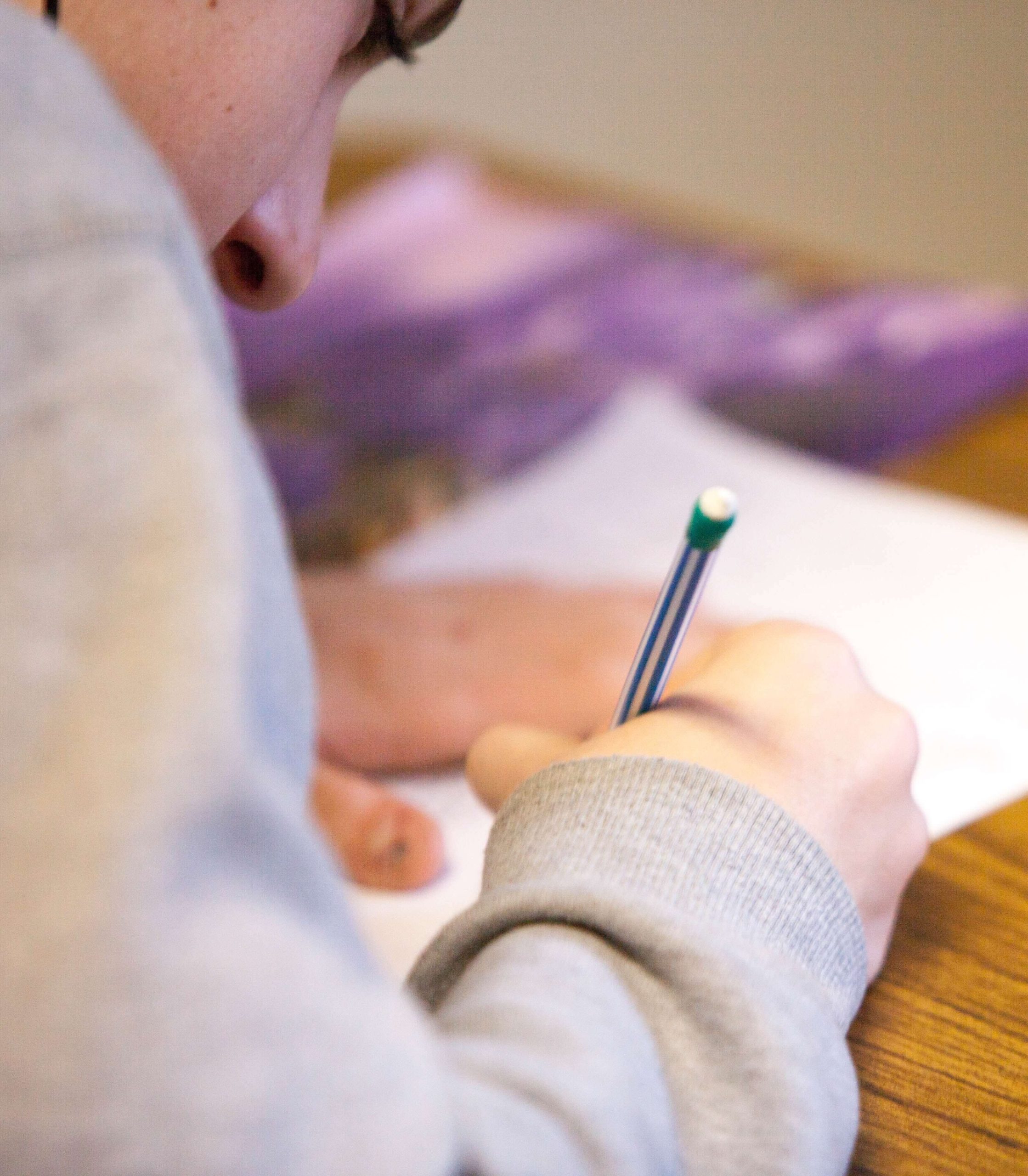A close-up of a child's hand writing in pencil on a sheet of paper.