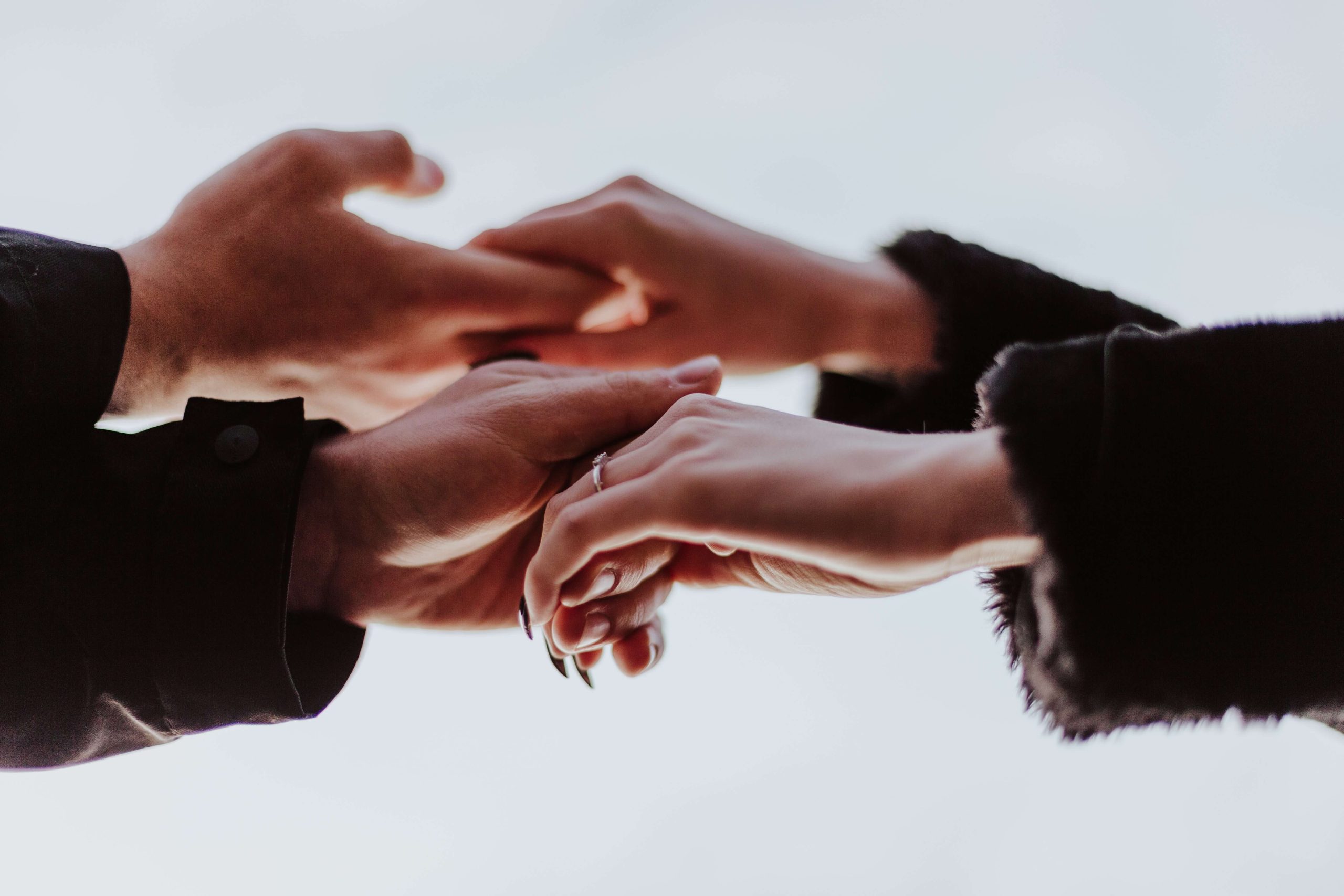 Several hands reaching towards one another against a pale background.