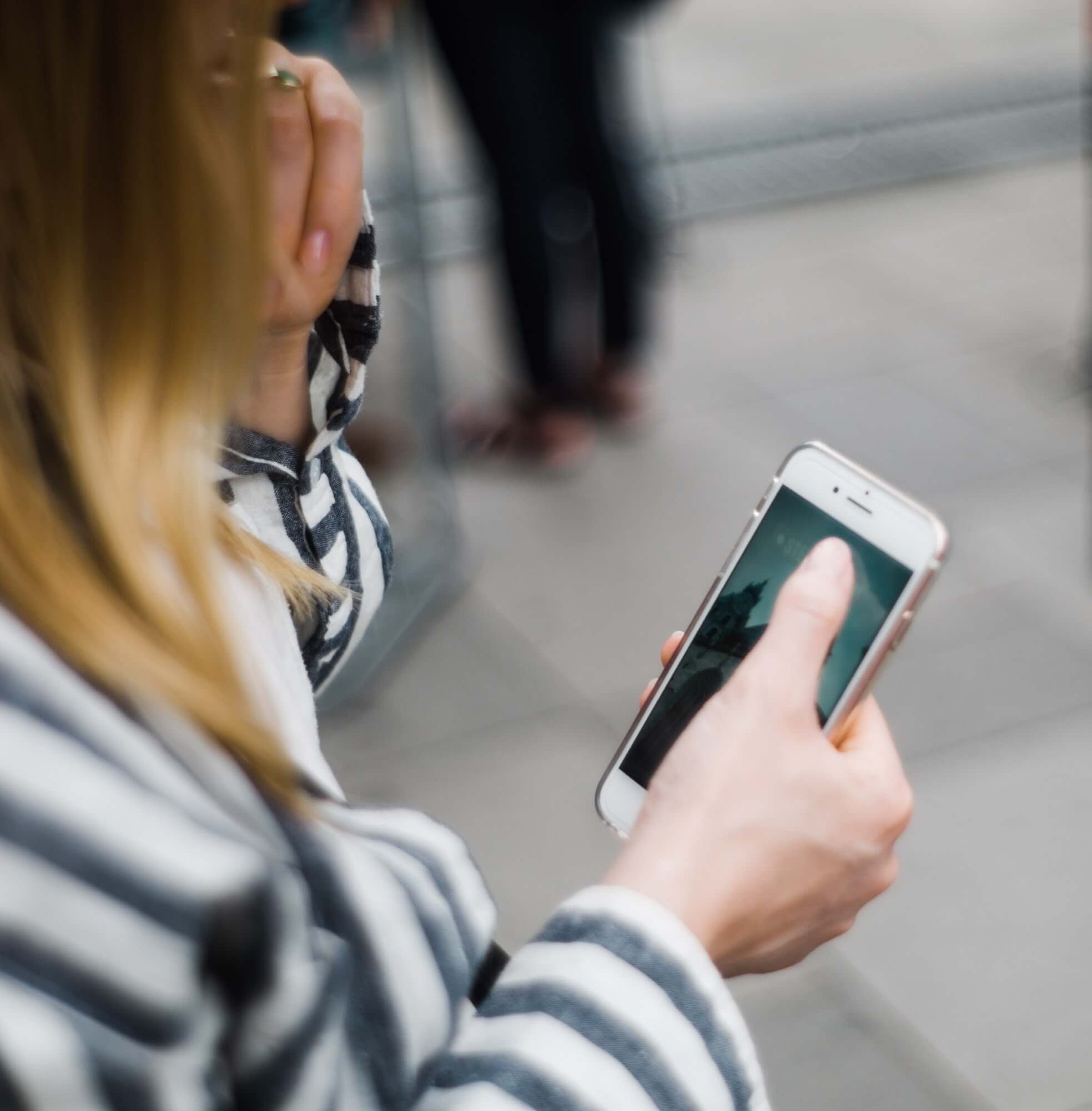 A person in a striped top holding up a phone, other people blurred behind them.