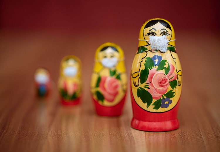 A row of Russian nesting dolls of decreasing size, each wearing a small face mask.