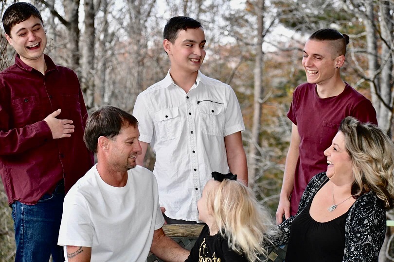 A family group standing outdoors among bare trees, talking and laughing together.