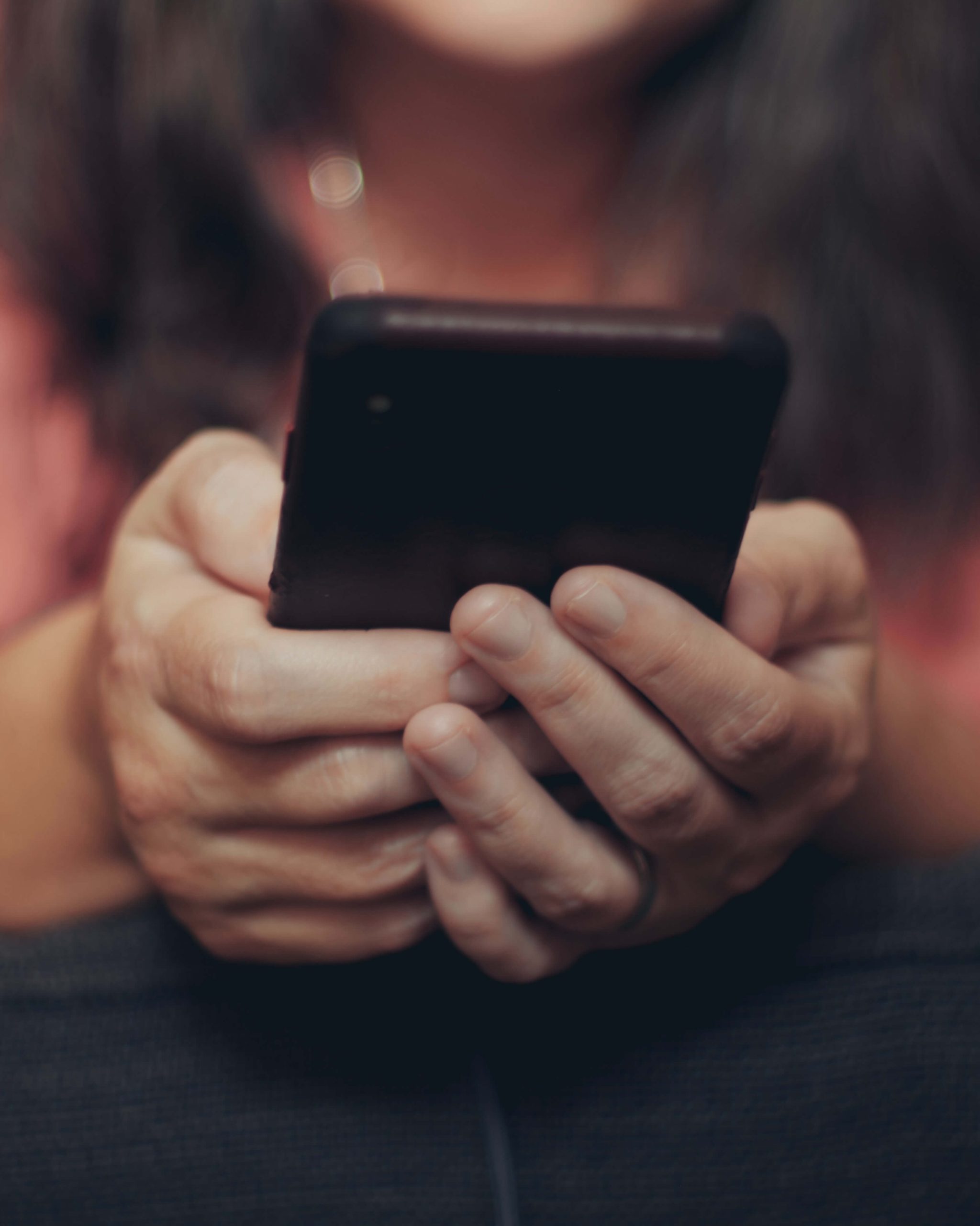 Close-up of a person's hands holding a mobile phone in their lap.