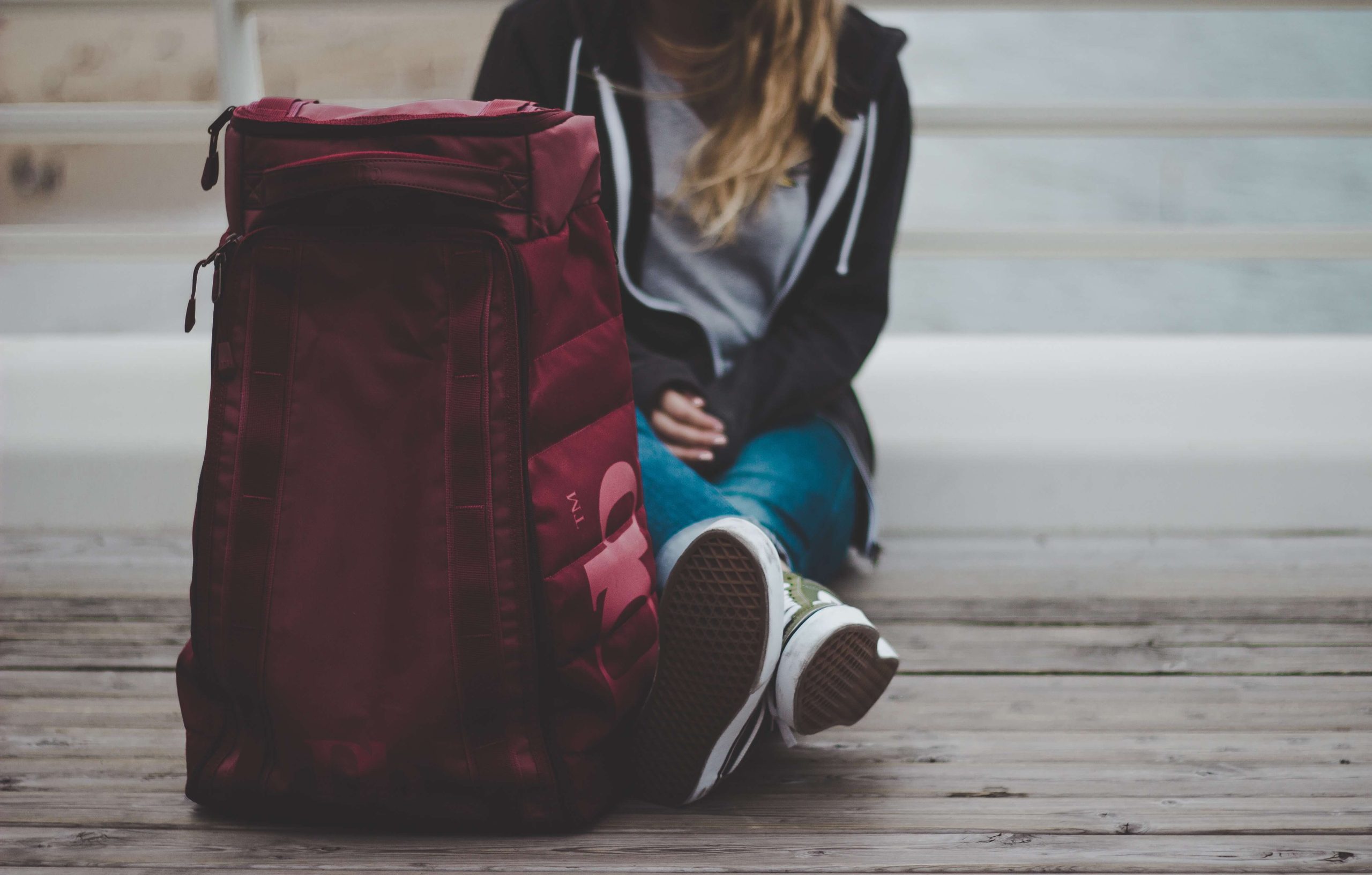 A girl sitting on bleacher steps beside a large red backpack, head bowed.