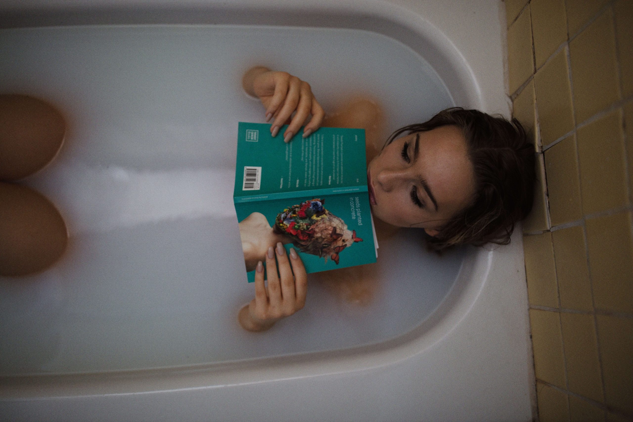 Overhead view of a person lying in a bath, reading a book.