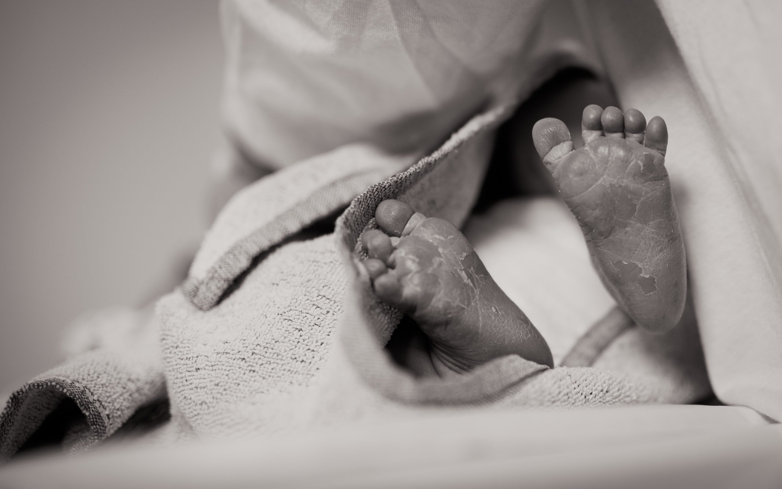 A black and white close-up of a newborn baby's feet on a blanket.