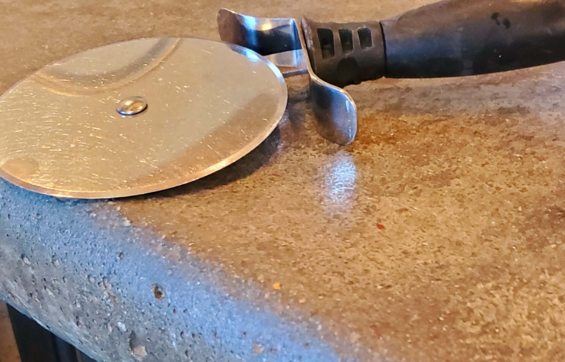 A pizza cutter resting on a wooden board on a kitchen counter.
