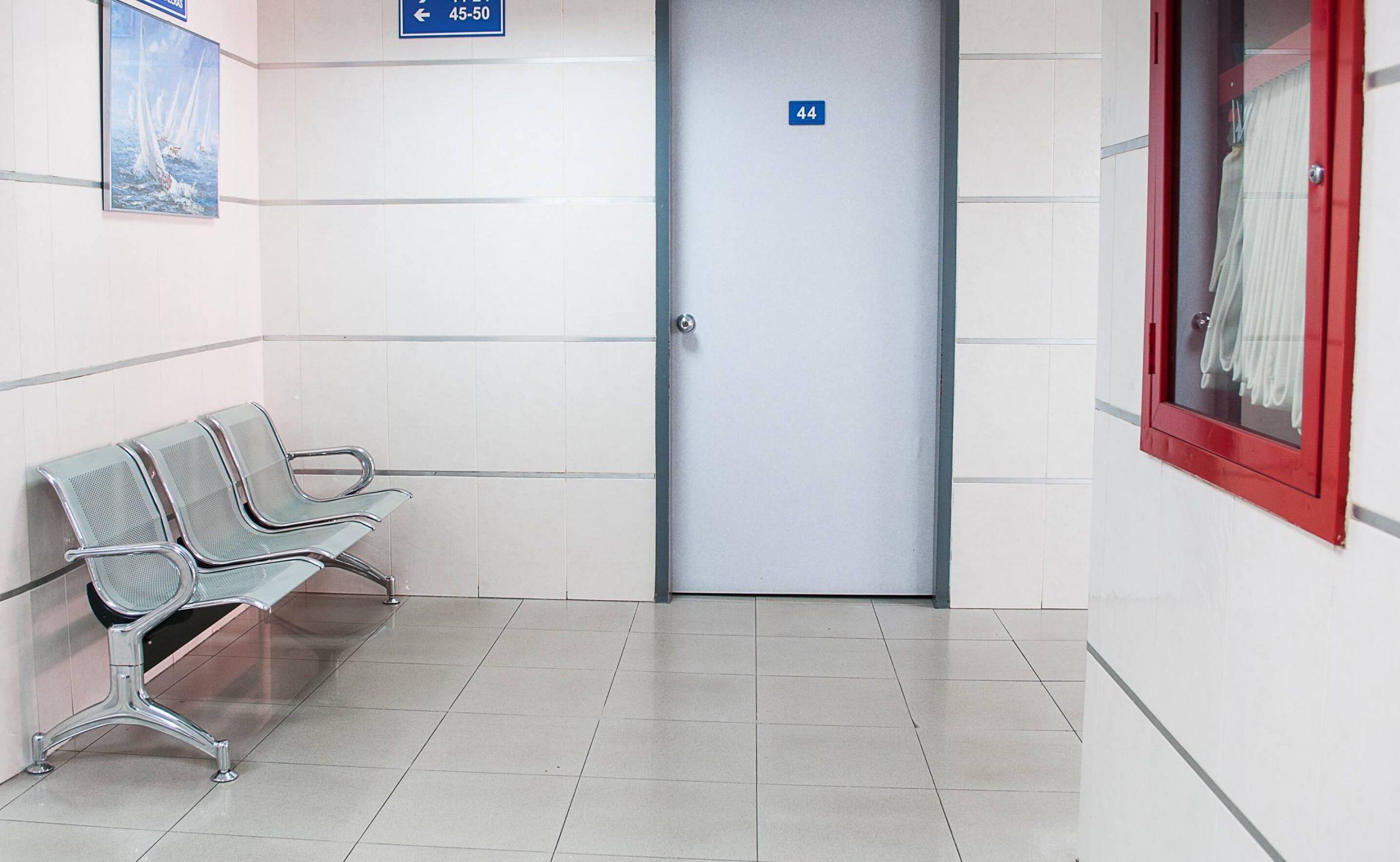 An empty hospital corridor with a row of chairs beside a closed door.