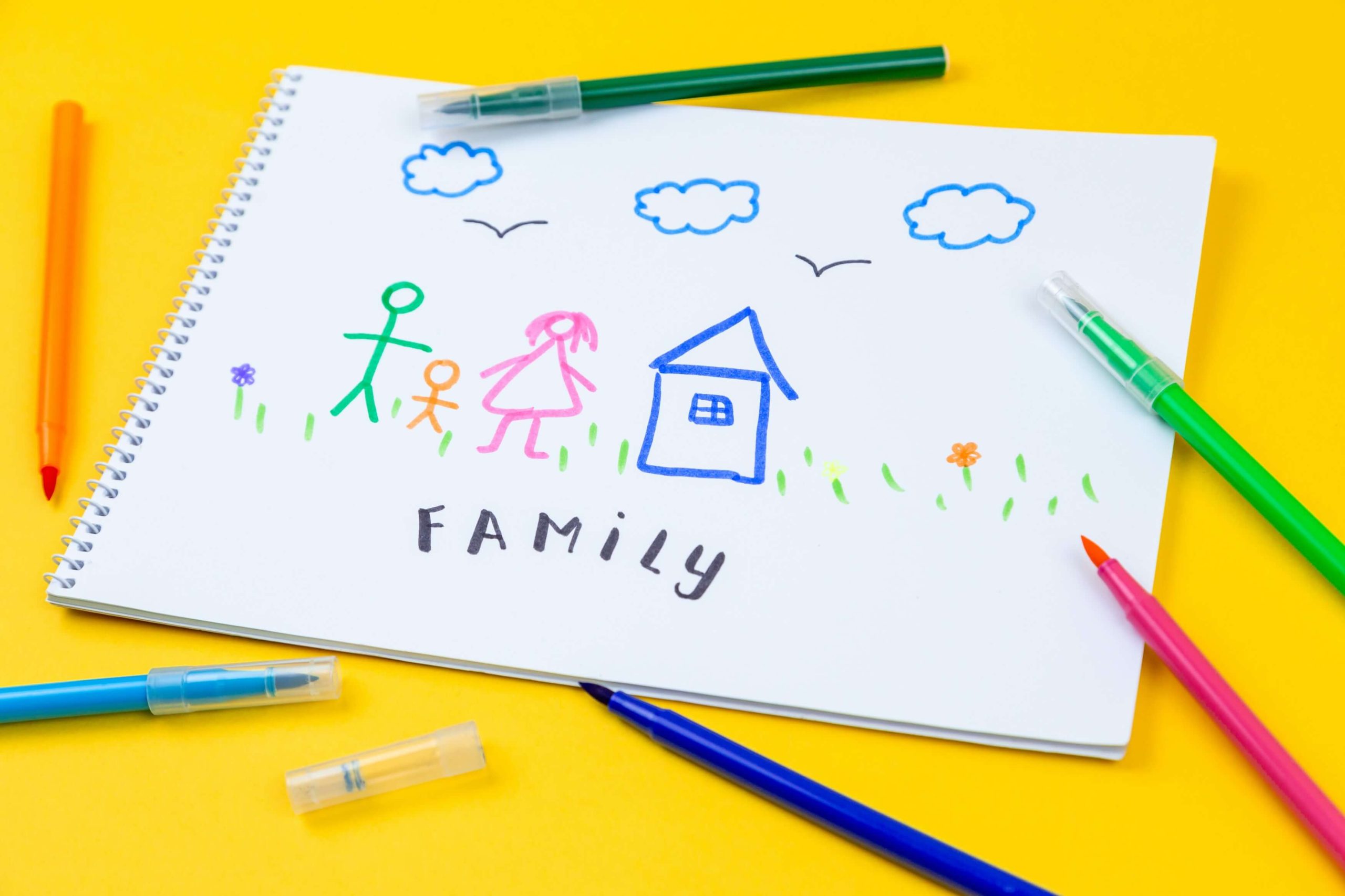 A child's felt-tip drawing of two adults, a child and a house, labelled "FAMILY", with pens scattered around it.