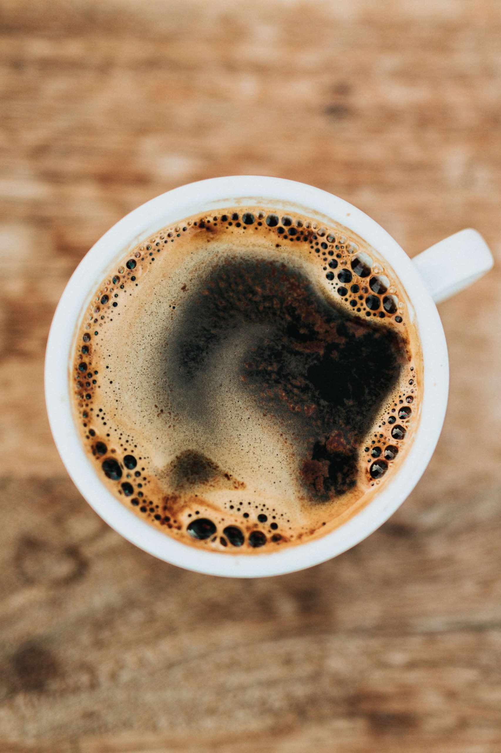 A cup of black coffee seen from above on a weathered wooden table.