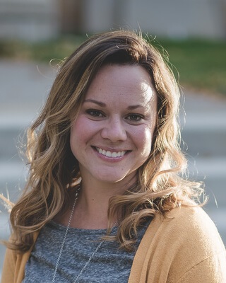 A woman with long wavy hair in a grey top and tan cardigan, smiling at the camera.