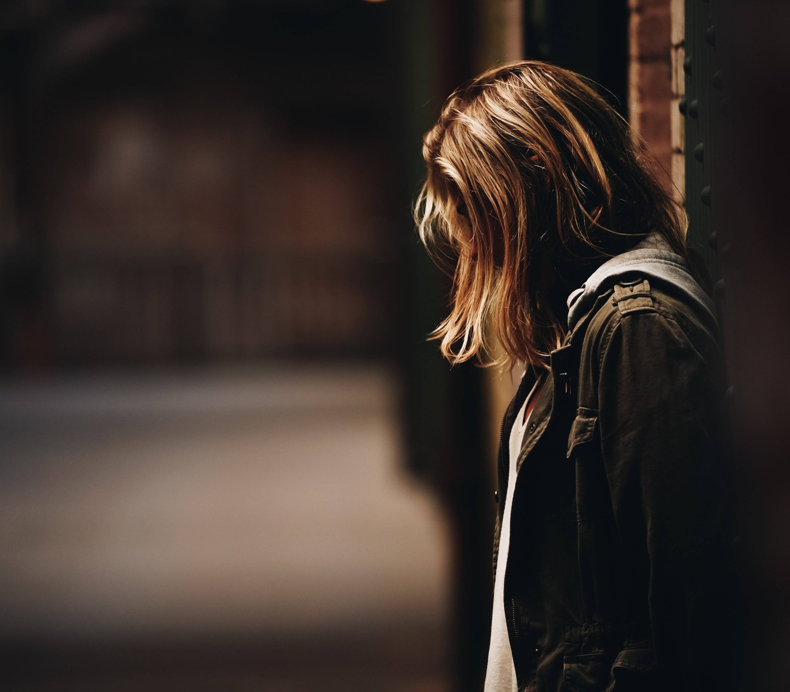 A young person with long hair standing in a doorway, head lowered, face turned away.