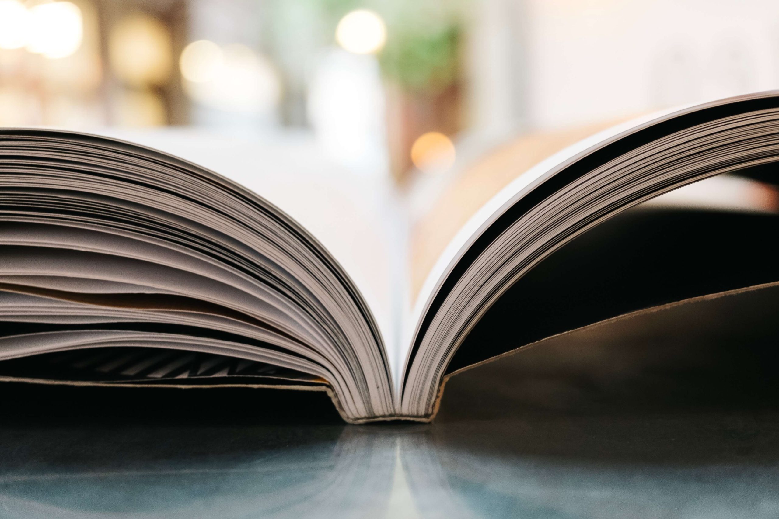 An open book resting on a reflective surface, pages fanned.