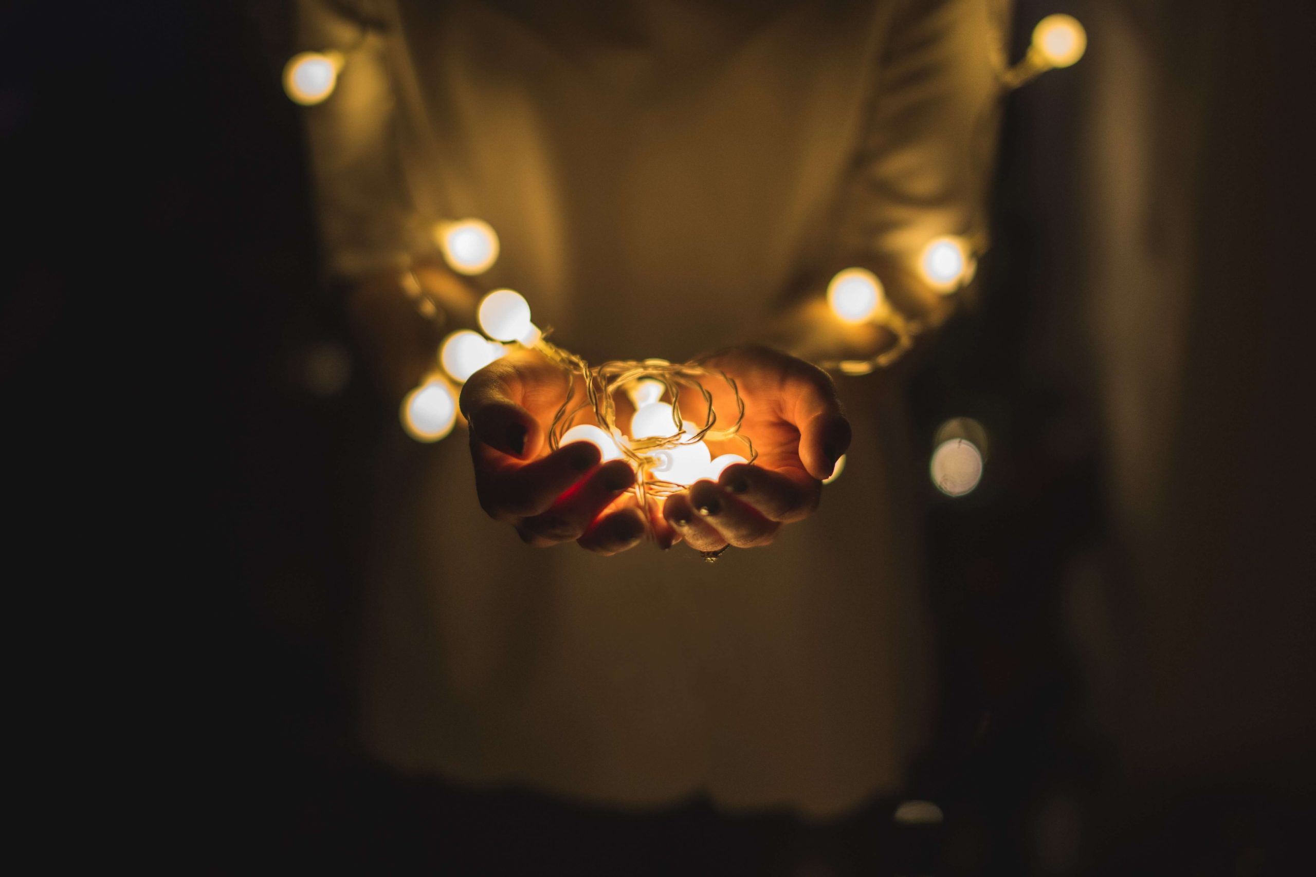 Cupped hands holding a small string of warm fairy lights in the dark.