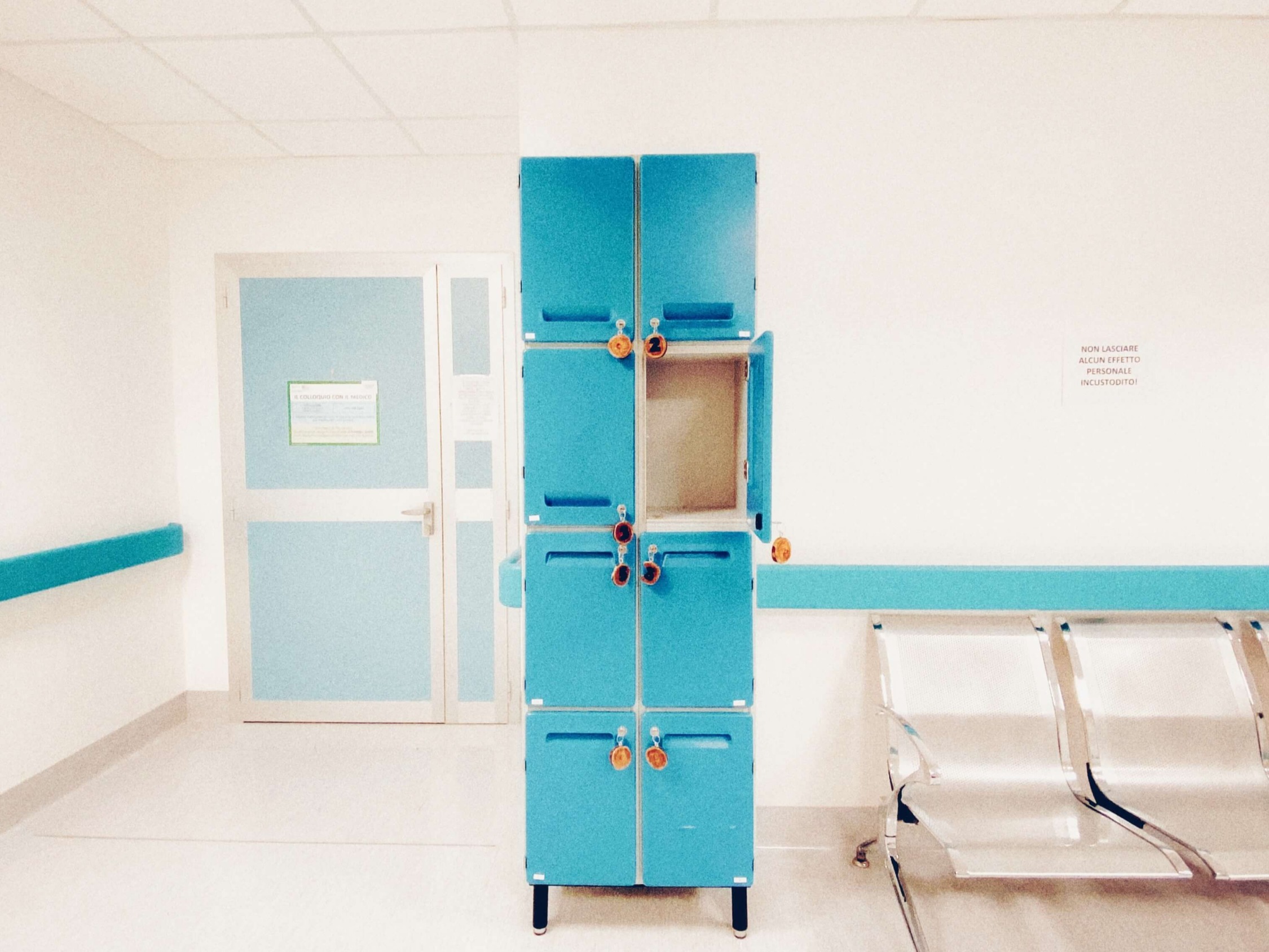 An empty clinic waiting area with a bank of blue lockers and a row of chairs.