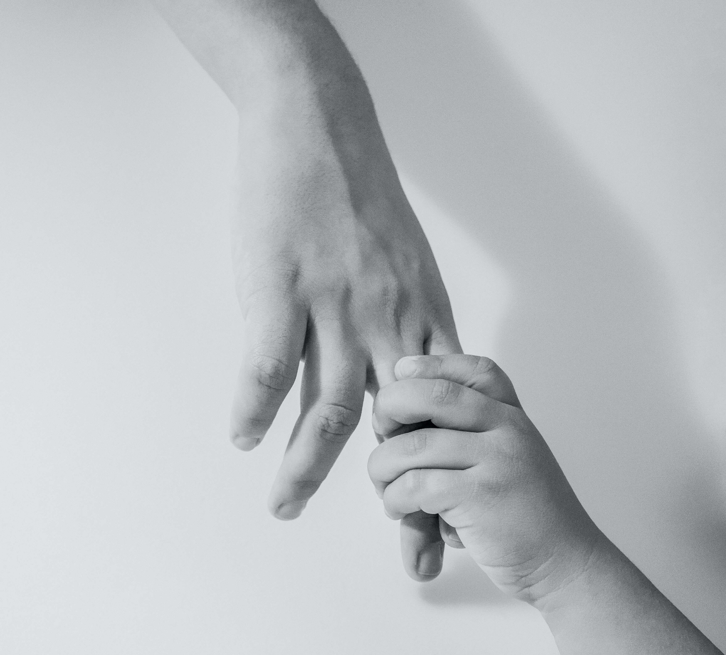 A black and white photograph of a small child's hand holding an adult's finger.