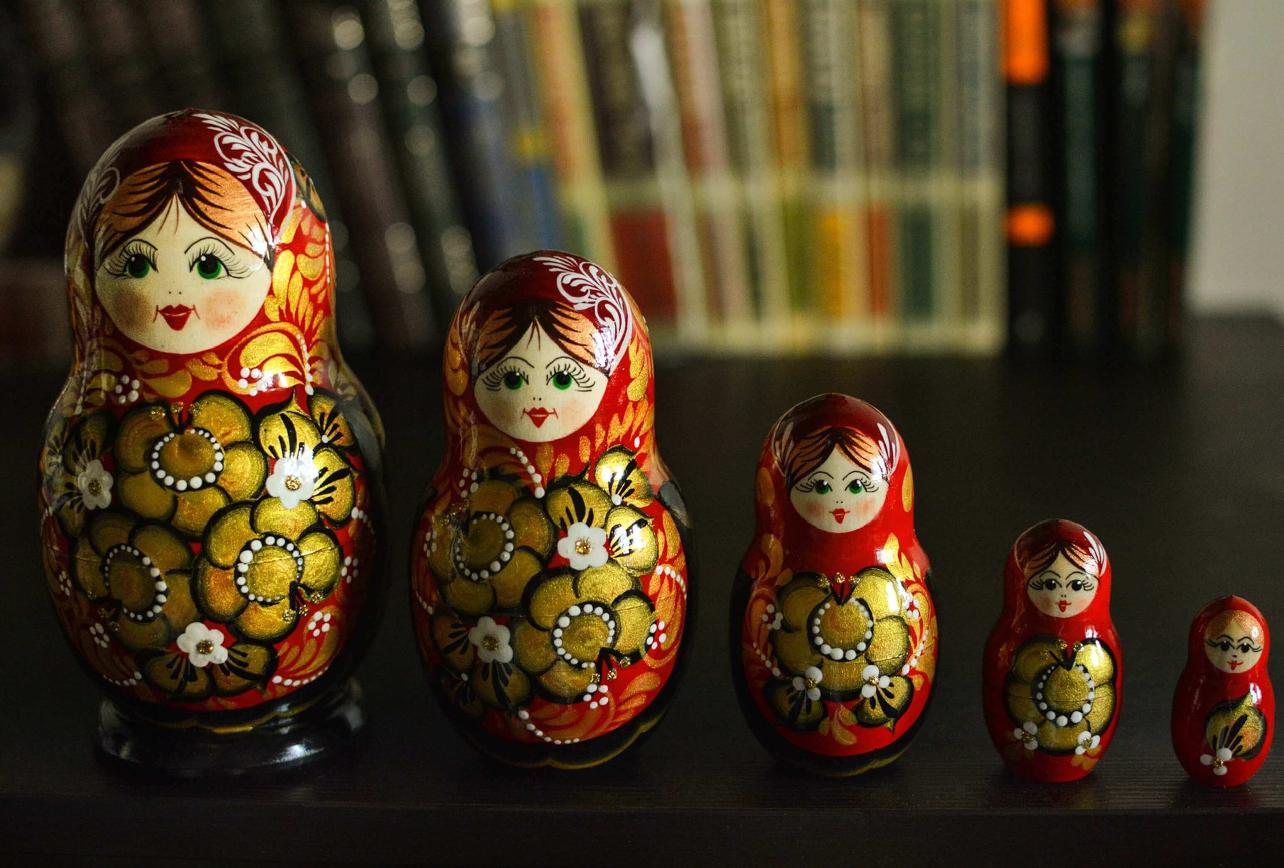 A row of painted Russian nesting dolls arranged from largest to smallest in front of a bookshelf.