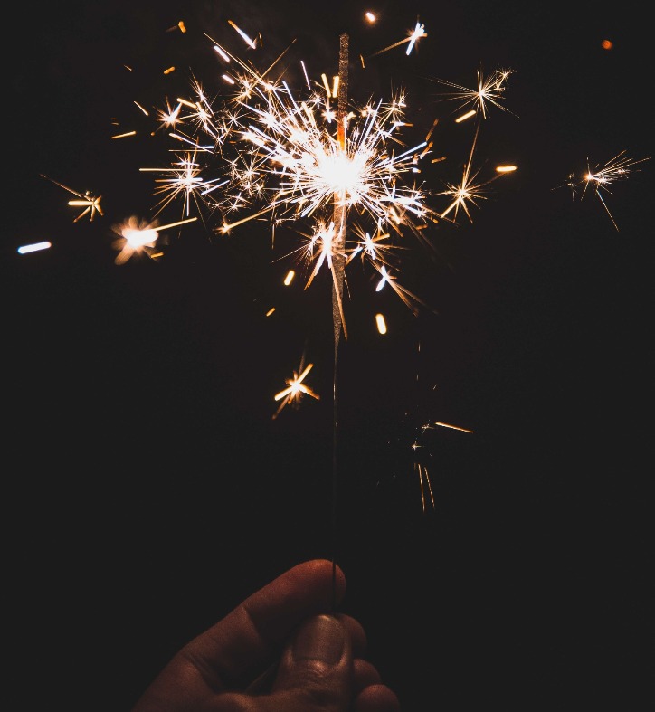 A hand holding a lit sparkler against a black background.