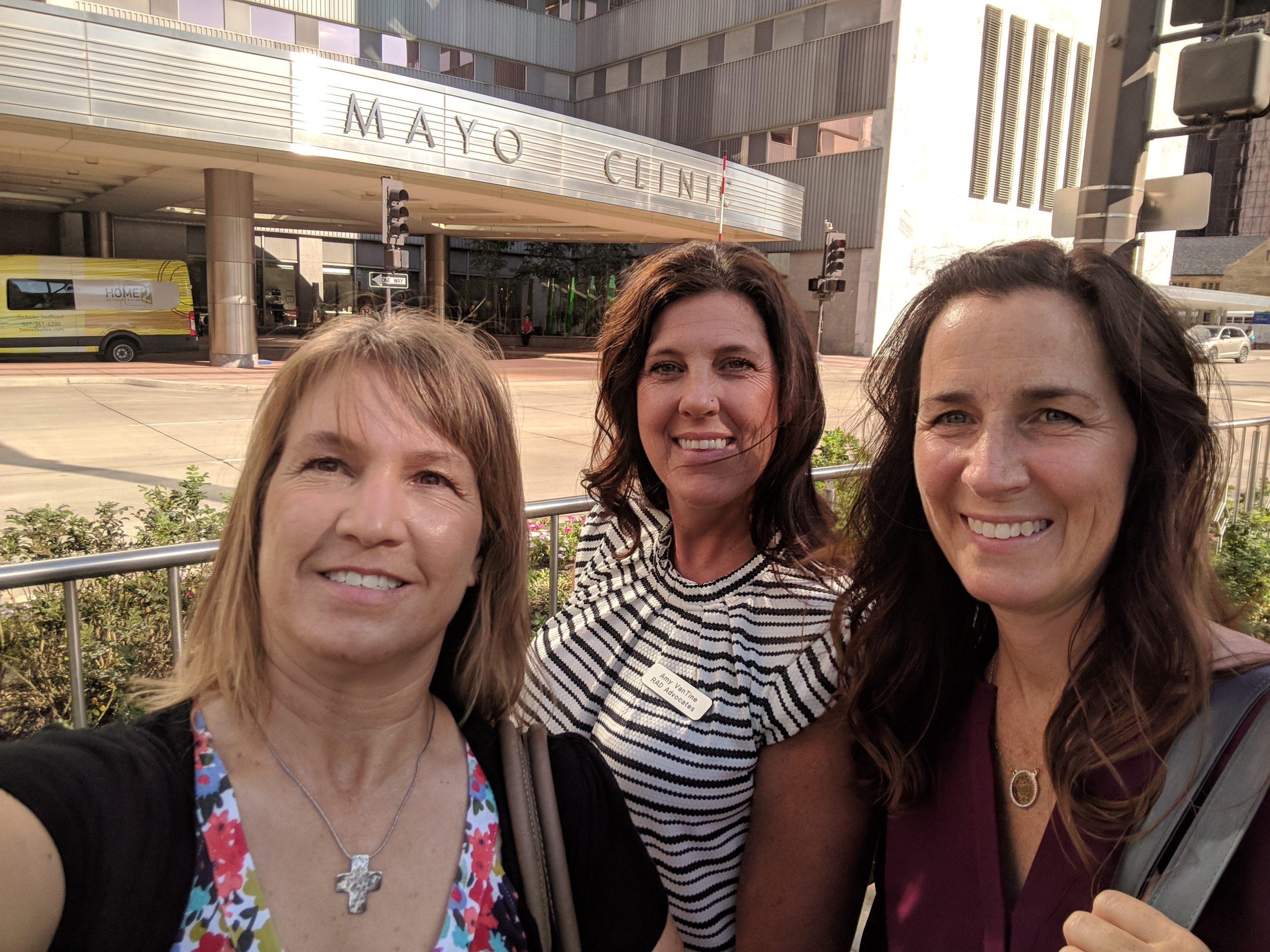 Three women smiling for a photograph outside a building signed Mayo Clinic.