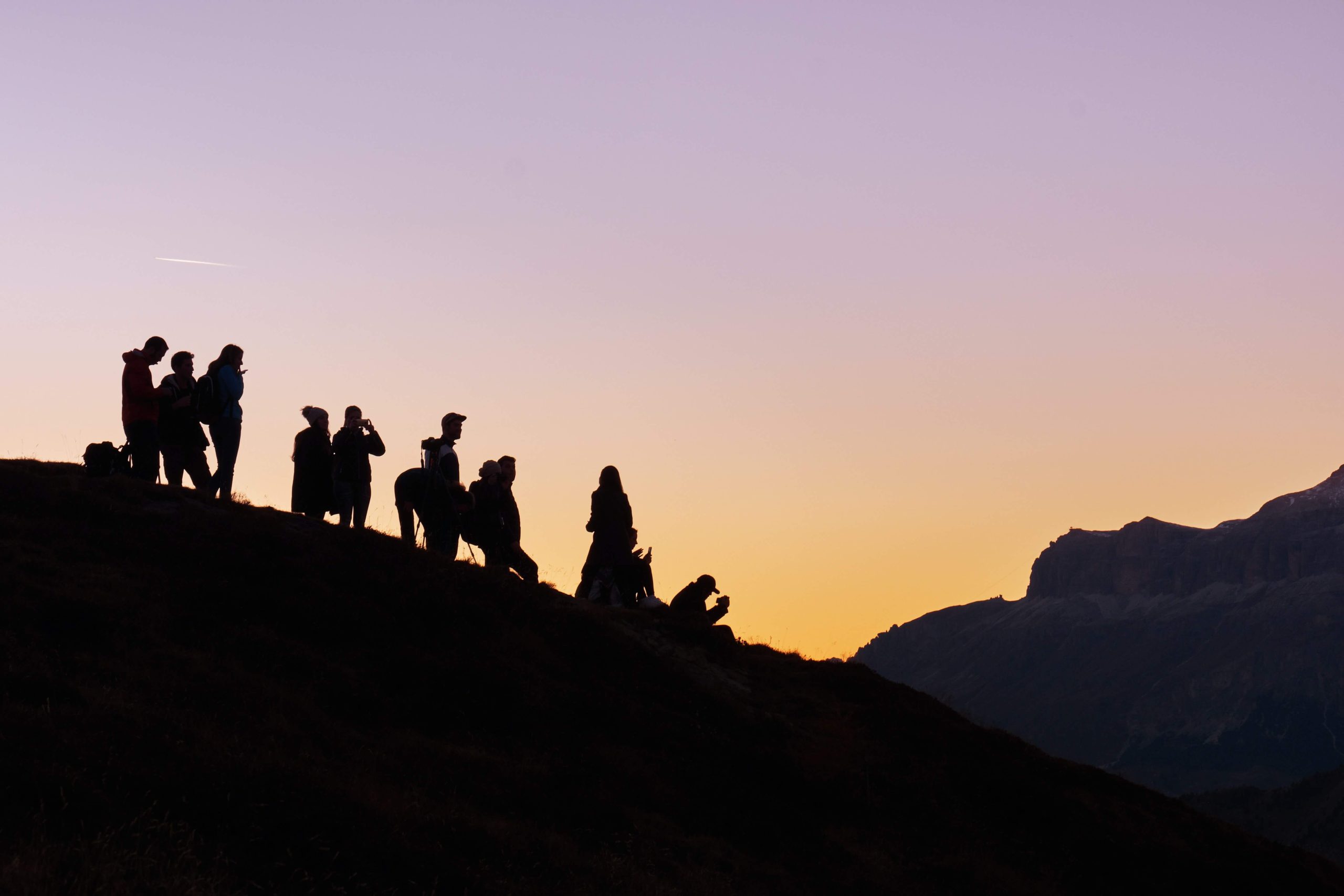 A group of people silhouetted on a hillside against a dusk sky.