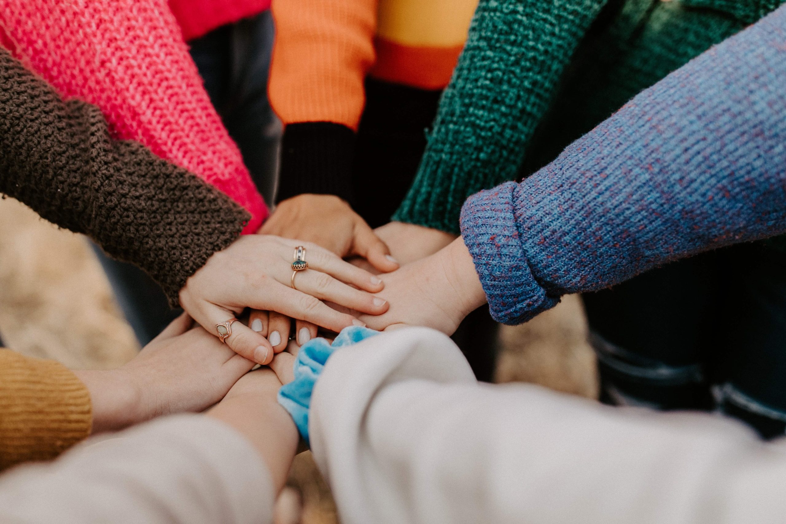A circle of people in colourful knitwear stacking their hands together in the middle.