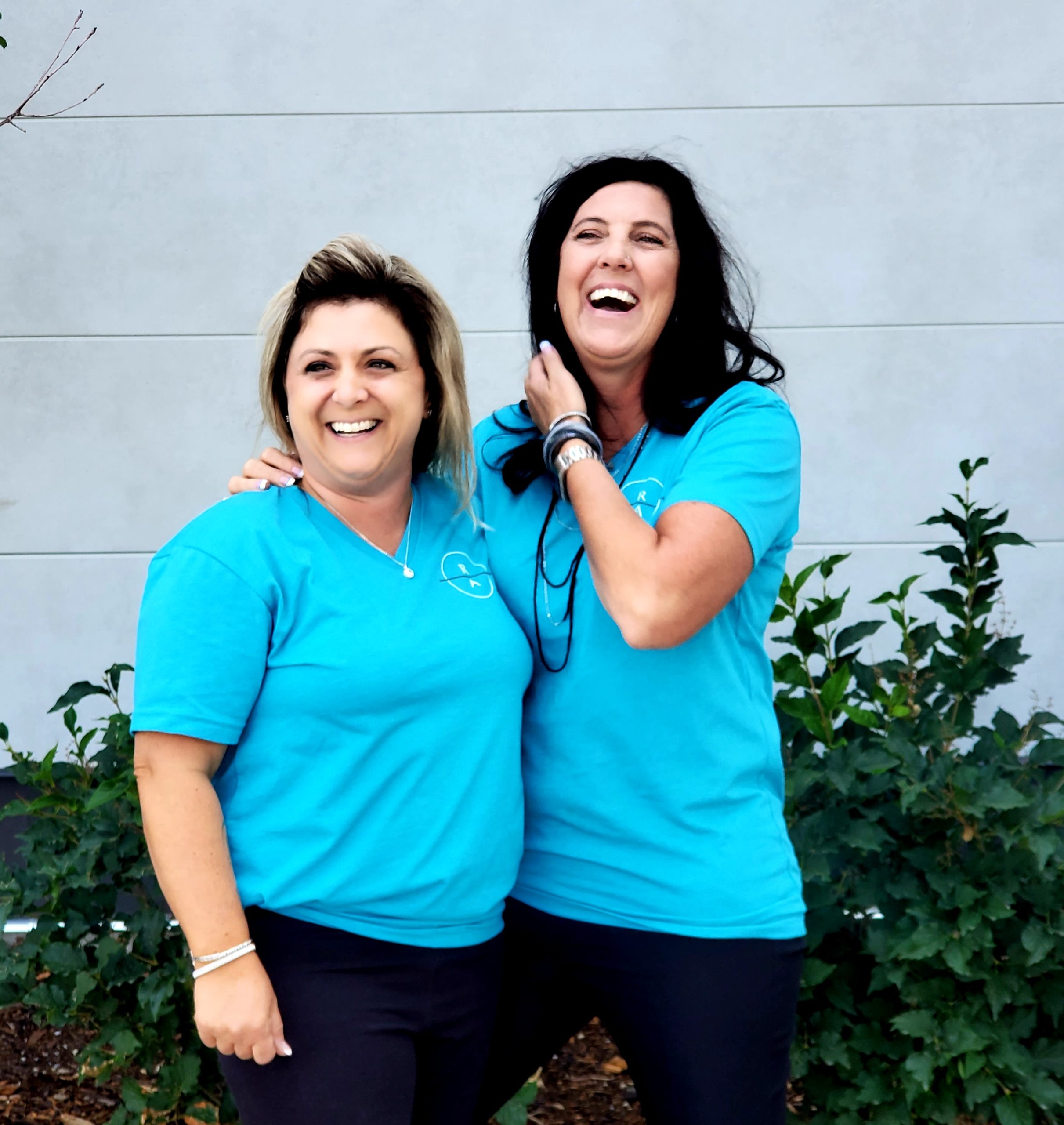Two women in matching bright blue polo shirts standing arm in arm, laughing.