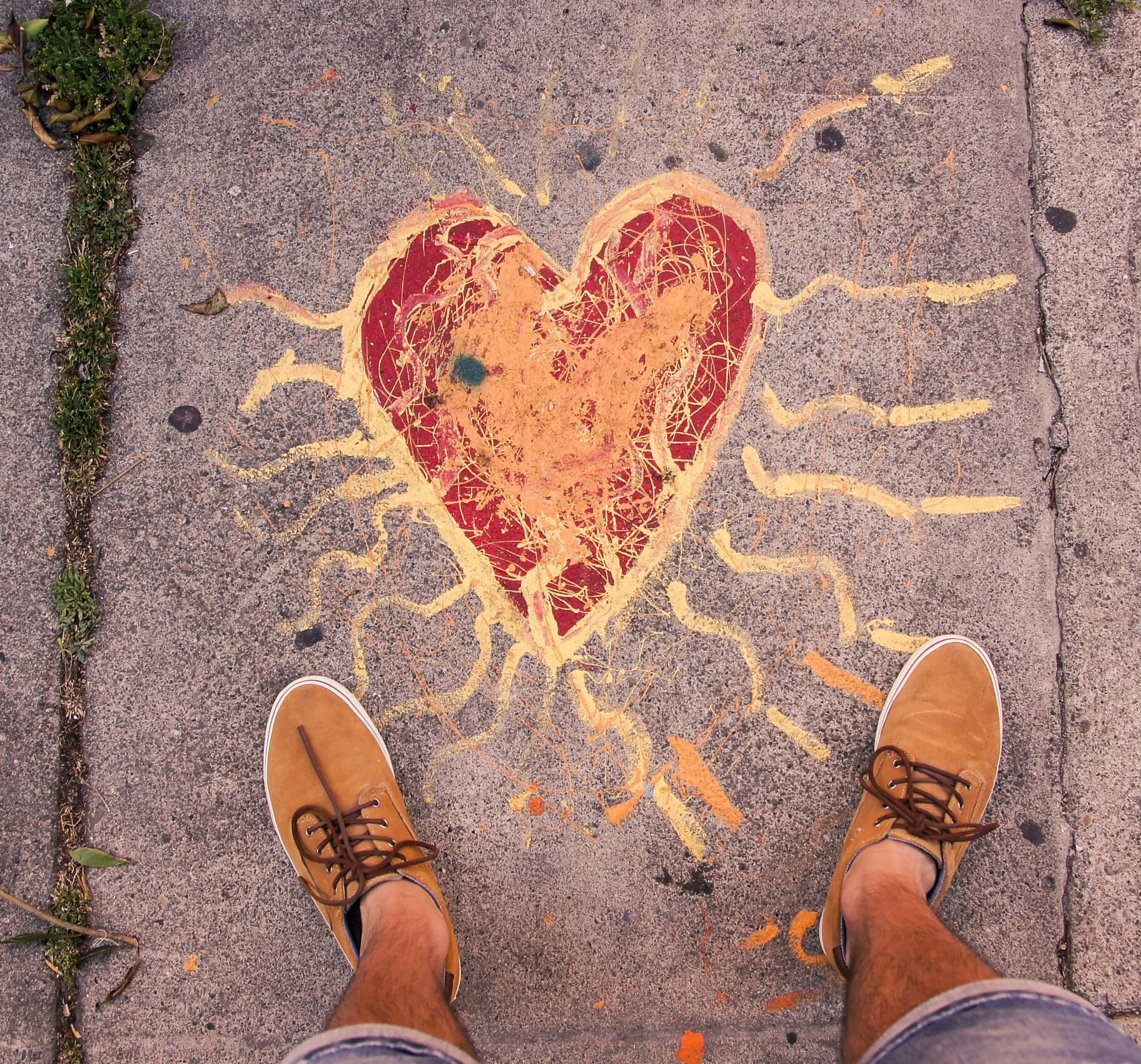 Looking down at a person's feet standing on a pavement painted with a large red and yellow heart.