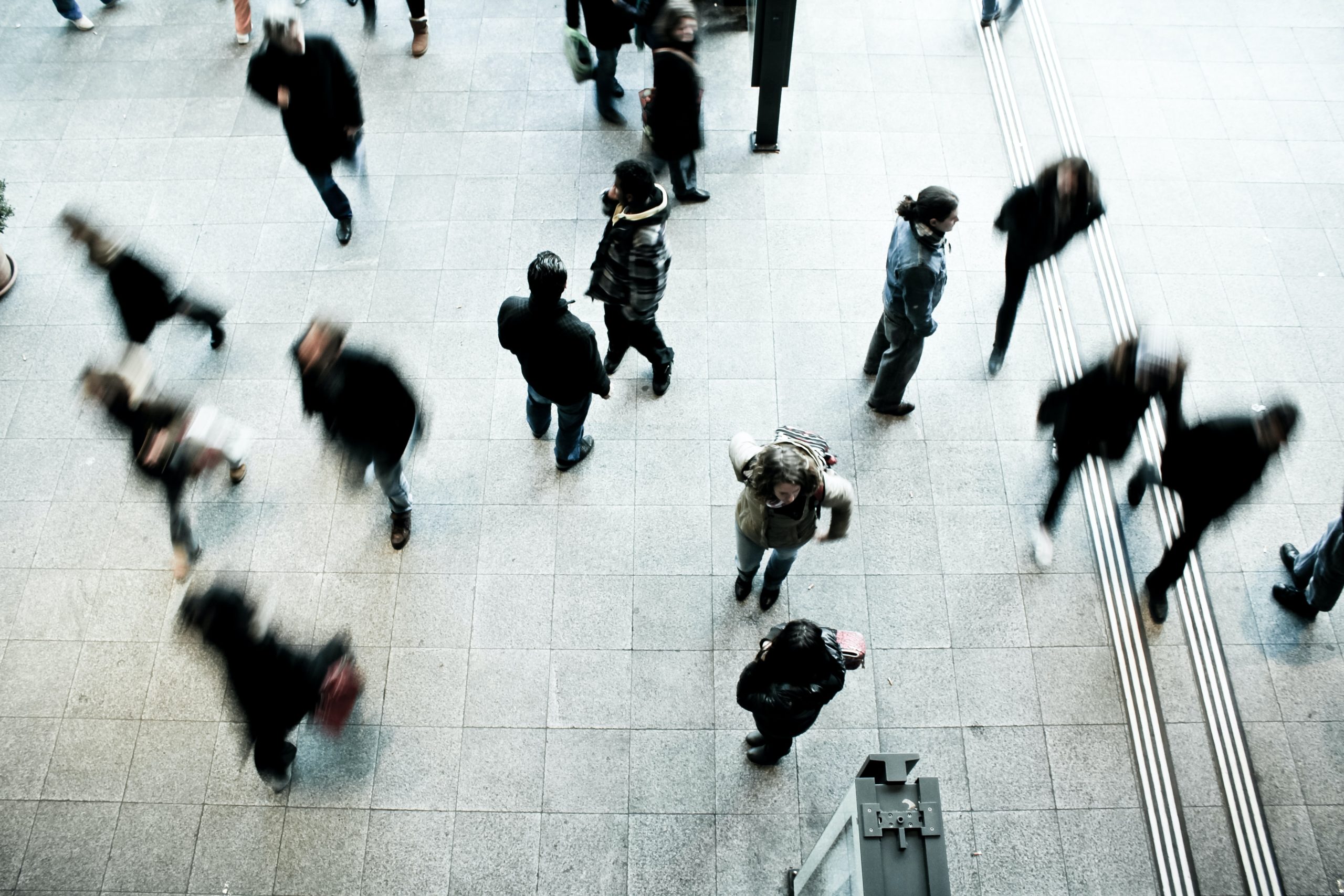 An overhead view of people crossing a pale floor, blurred by motion.