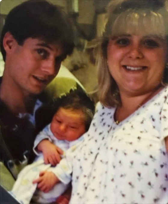 A young couple holding their newborn baby, smiling for the camera.